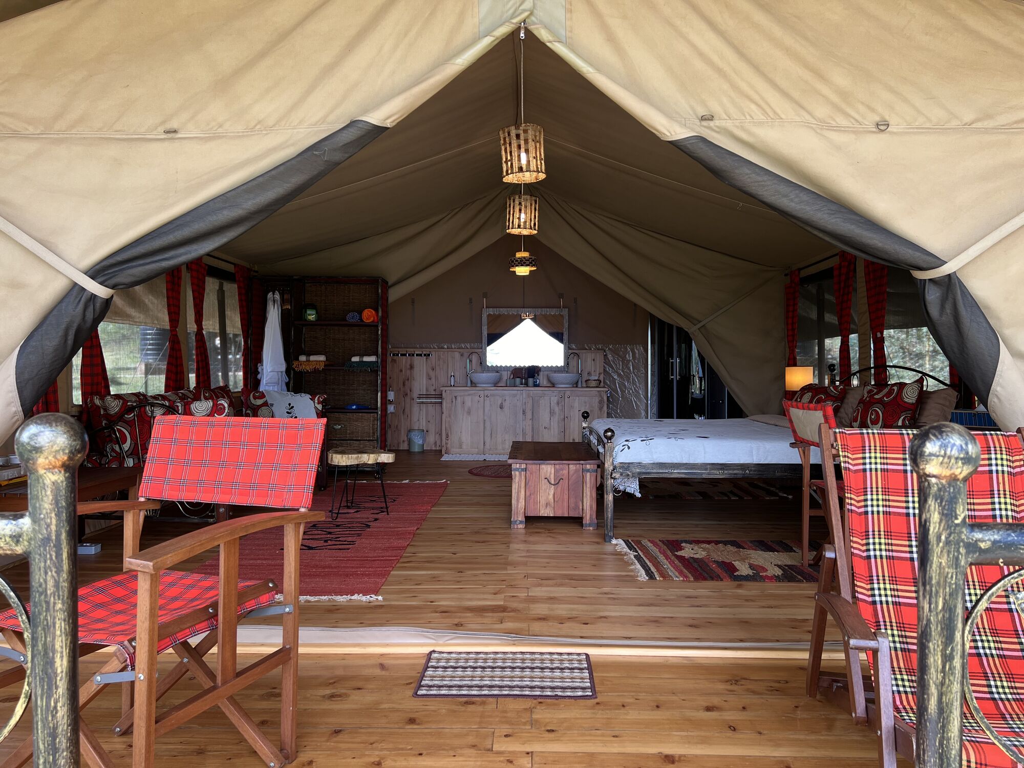 Inside a safari tent with wooden floors, red woven chairs and a bed